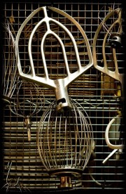 Various metal mixing whisks displayed on a wire grid, featuring different shapes and sizes.