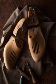 Two wooden shoe forms placed on a piece of leather with carving tools nearby.