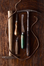Collection of hand tools including a wooden mallet, chisels, and a leather strap on a wooden surface.