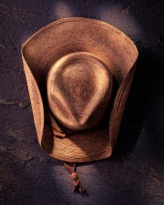 A brown straw hat with a wide brim and a decorative cord hanging from the base.